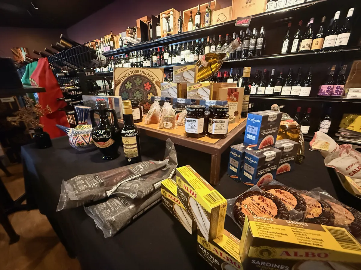 The food table at La Vid: packs of chorizo and salchichón, tins of Albo sardines, jars, olive oil, and boxed sweets, with wine shelves behind