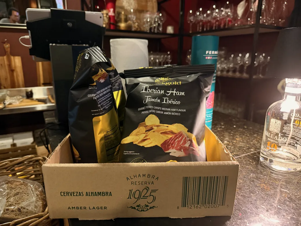 Bags of Iberian ham flavored potato chips in an Alhambra beer box on the counter at La Vid