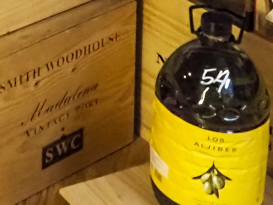 A large yellow-labeled jug of Los Aljibes olive oil on a wooden port crate at La Vid