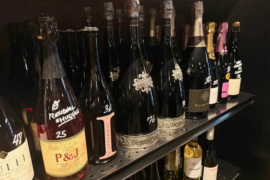 La Vid’s sparkling shelf: rows of Cava and other sparkling bottles, with handwritten prices and notes on several