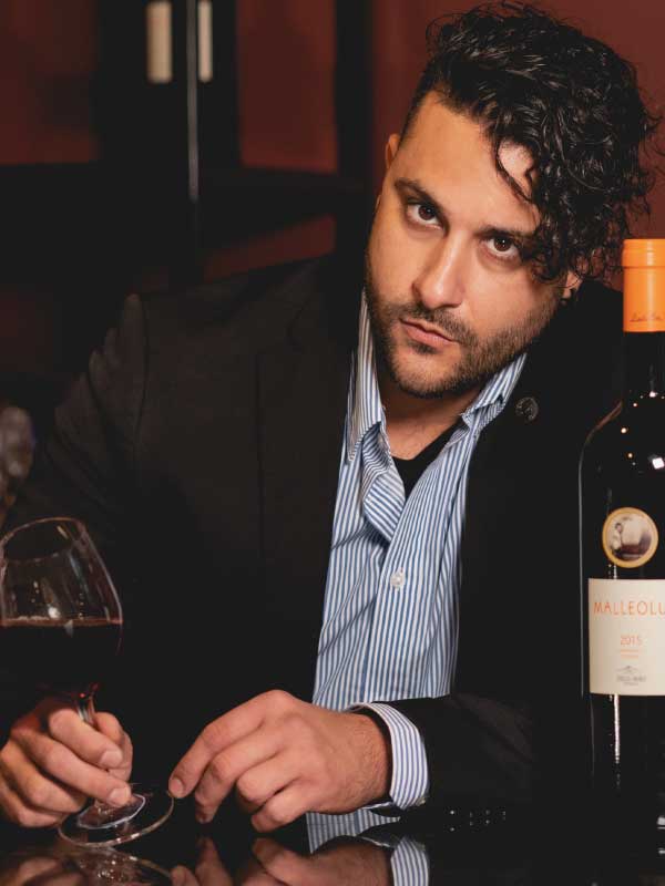 Victor seated at the bar with a glass of red wine and a bottle beside him