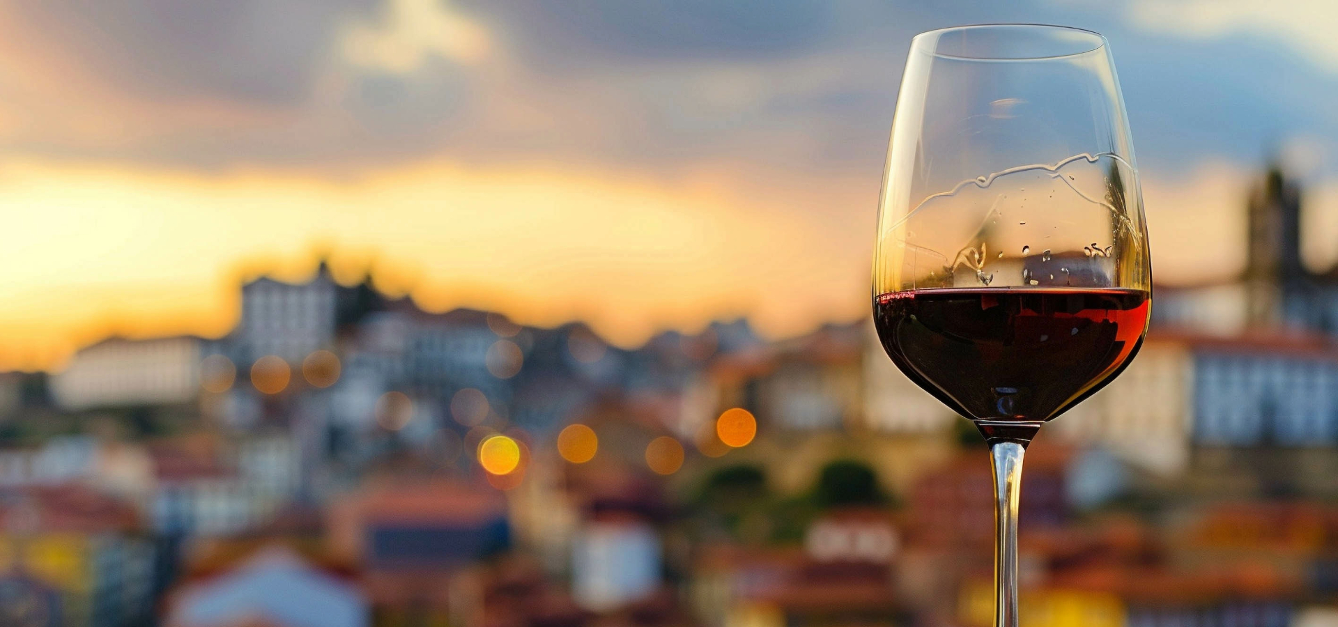 A glass of red wine at sunset above the rooftops of Porto