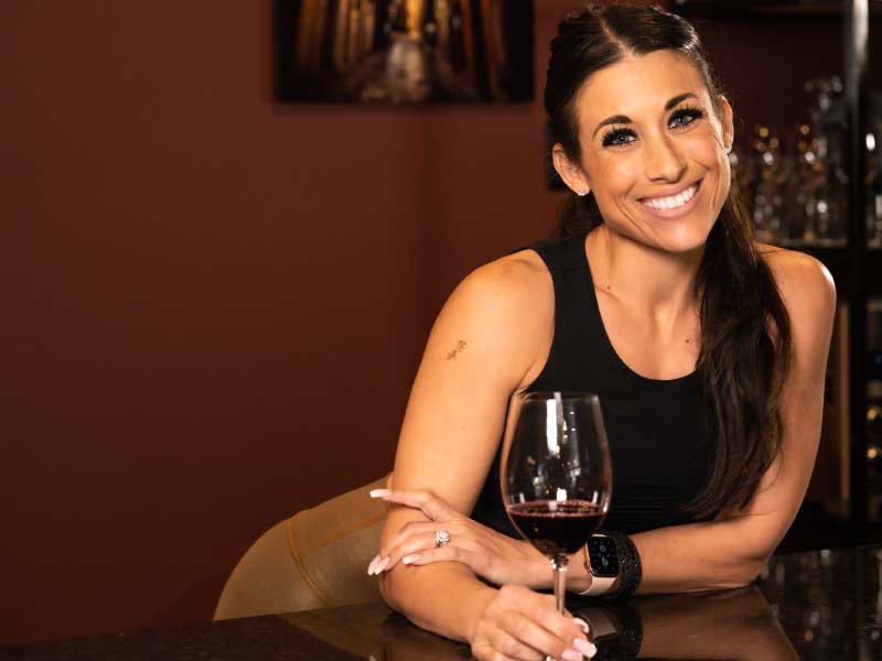 A guest smiling at the bar of La Vid with a glass of red wine